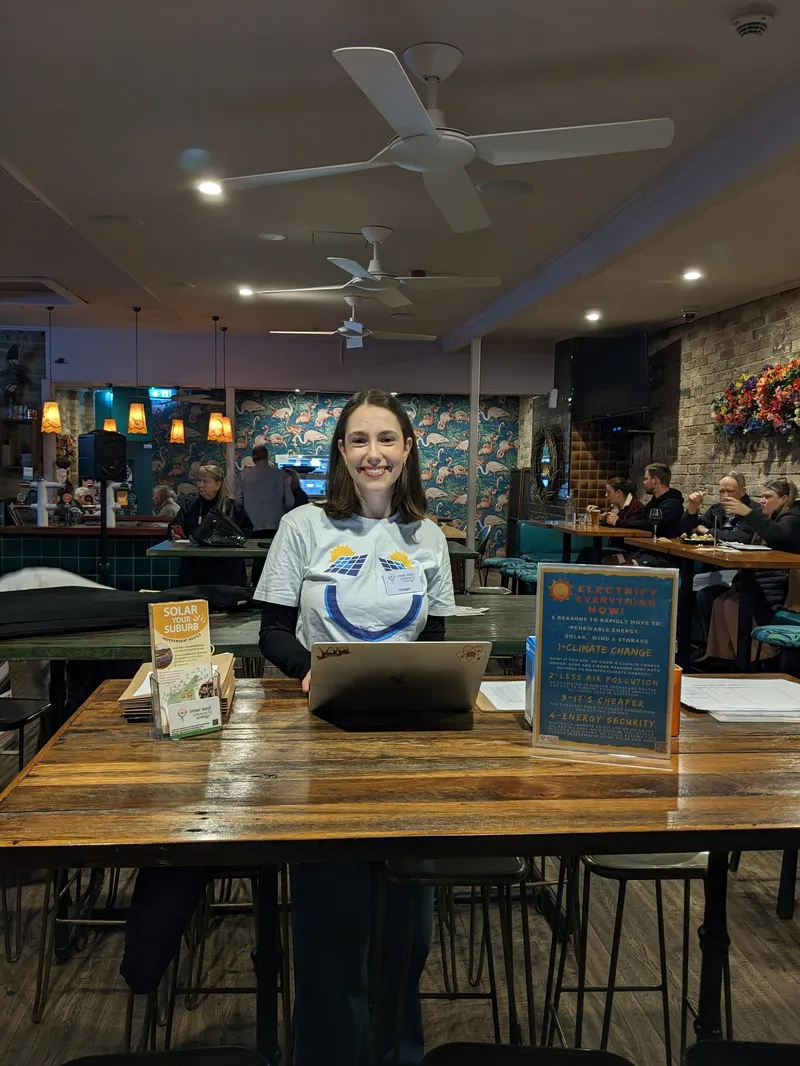 A smiling volunteer at a table with a laptop and brochures in a Balmain pub