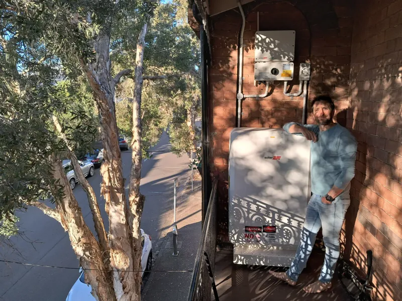 Josh leaning on his new home battery on a balcony