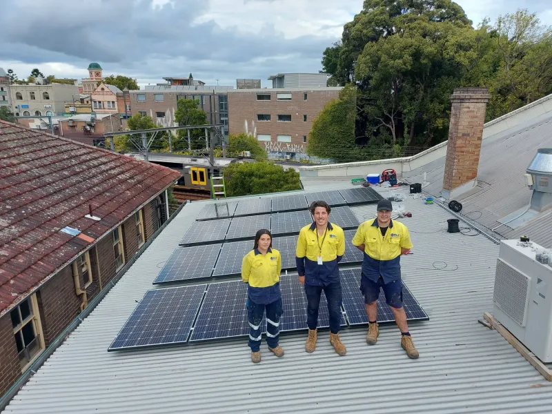 Three installers in hi-vis shirts standing among solar panels on a roof