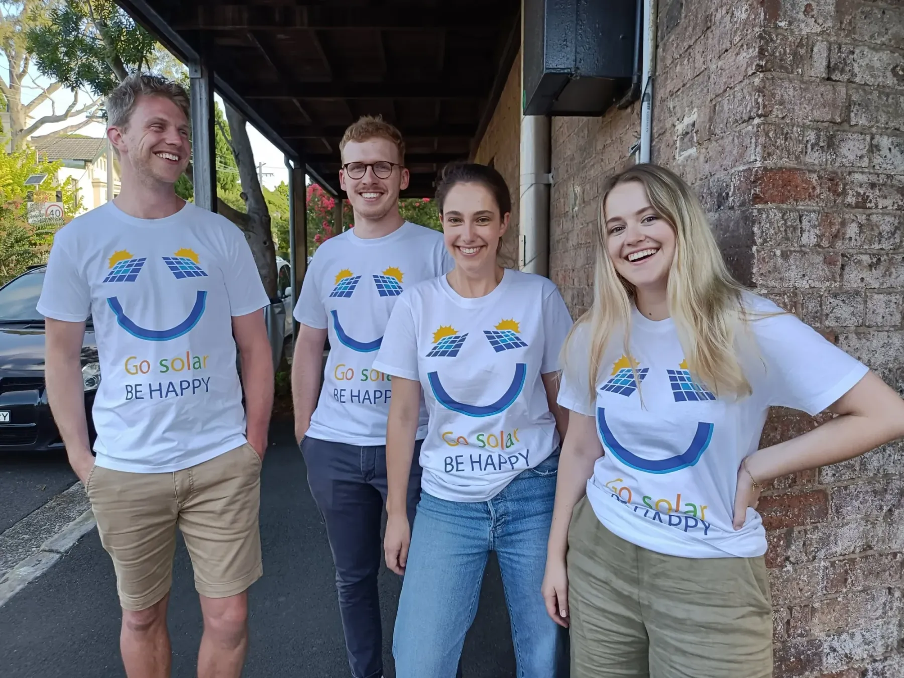 Four smiling IWCE volunteers wearing white Go solar, be happy T-shirts