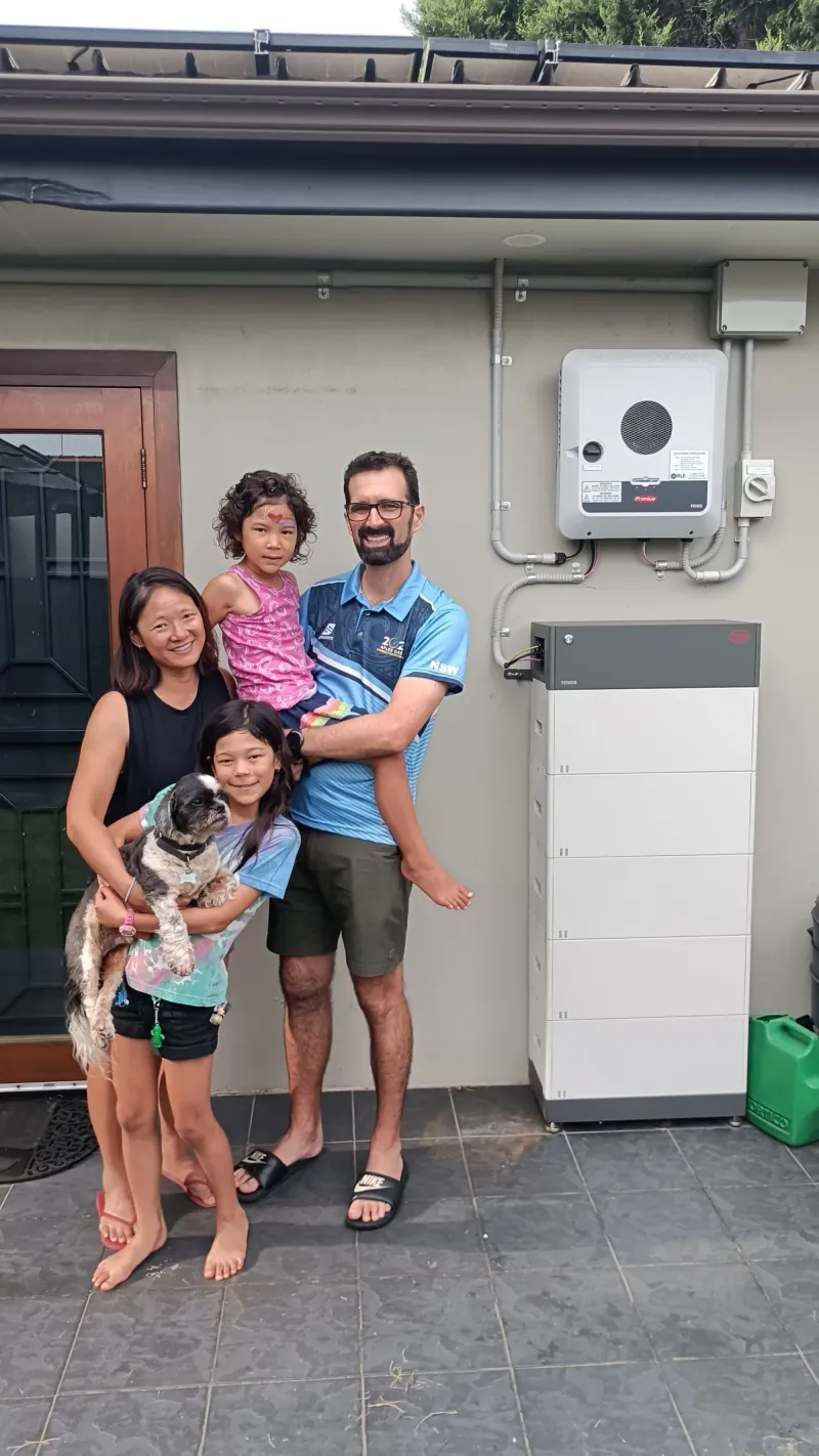 Alice, Owen, their two children and dog in front of their solar inverter and battery