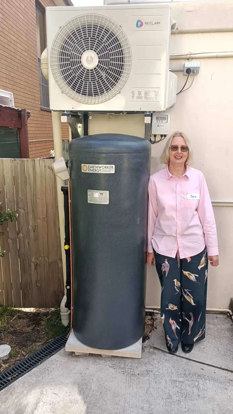 Ses standing beside a heat pump hot water tank with its fan unit mounted above