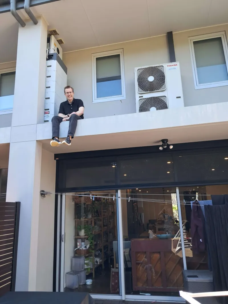Chris sitting on a ledge beside his air conditioner and home battery