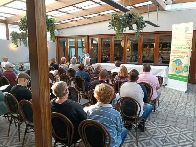 People seated in a pub courtyard listening to a speaker
