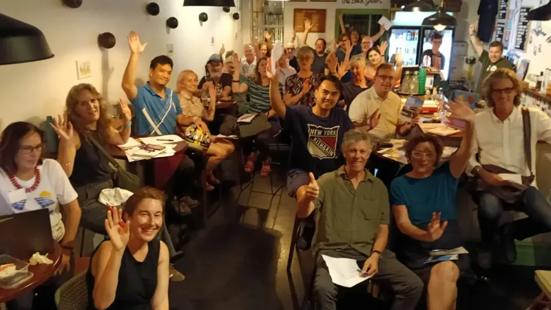 A packed room with hands raised at an Info Event