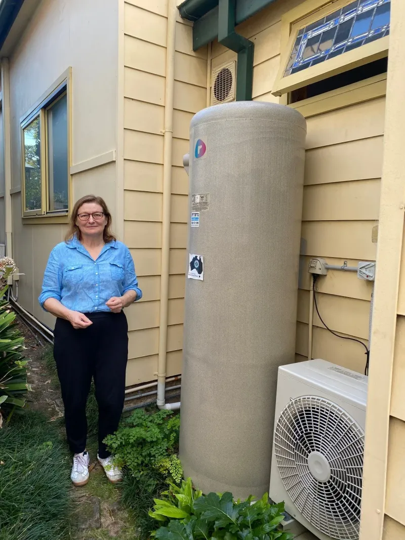 Carmen standing beside her new heat pump hot water tank