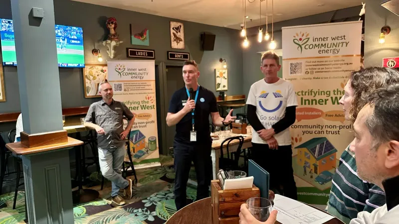 Three speakers in front of Inner West Community Energy banners at a pub