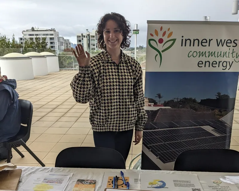 A smiling volunteer waving from behind an Inner West Community Energy stall