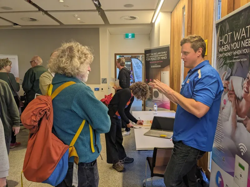 Tye talking with a visitor at a hot water heat pump stall